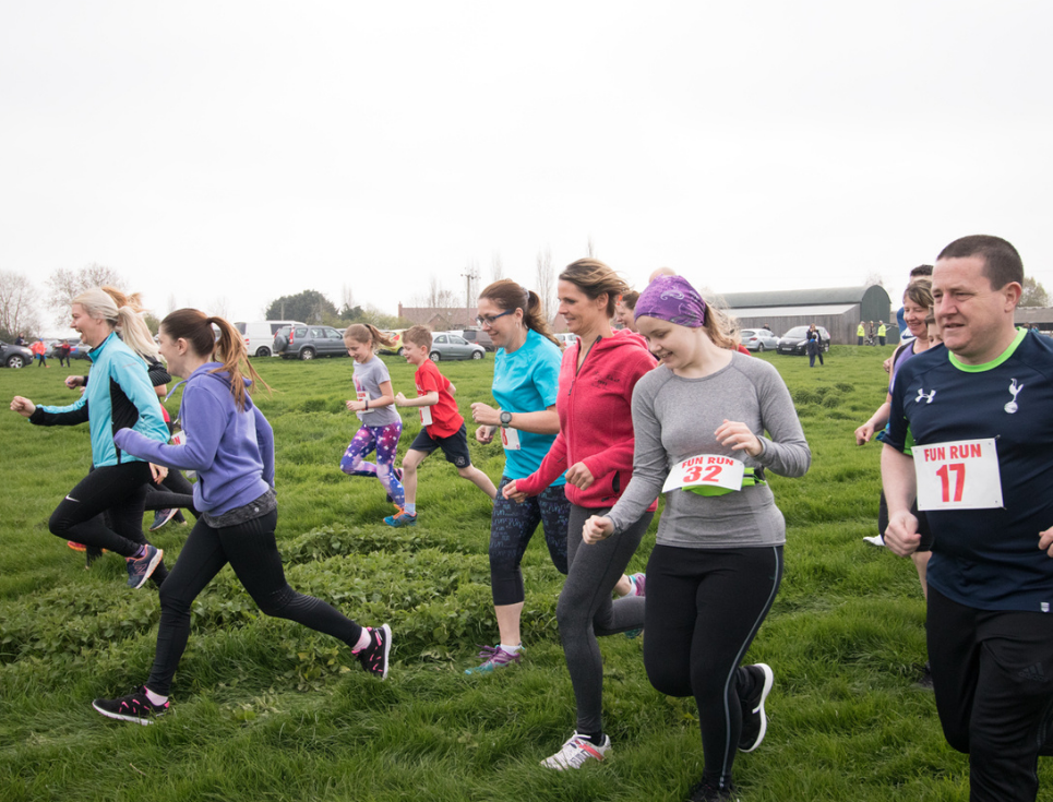 Runners wearing racing number labels jogging across grassland