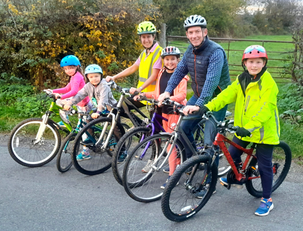 A group of children and adults pictured standing with their bicycles. Everyone is wearing a helmet.