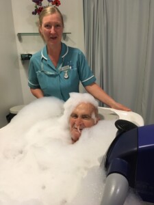 Healthcare Assistant Clarissa, with Leslie Salmon in a bath completely filled with white fluffy bubbles. You can only see Leslie's head above the bubbles.