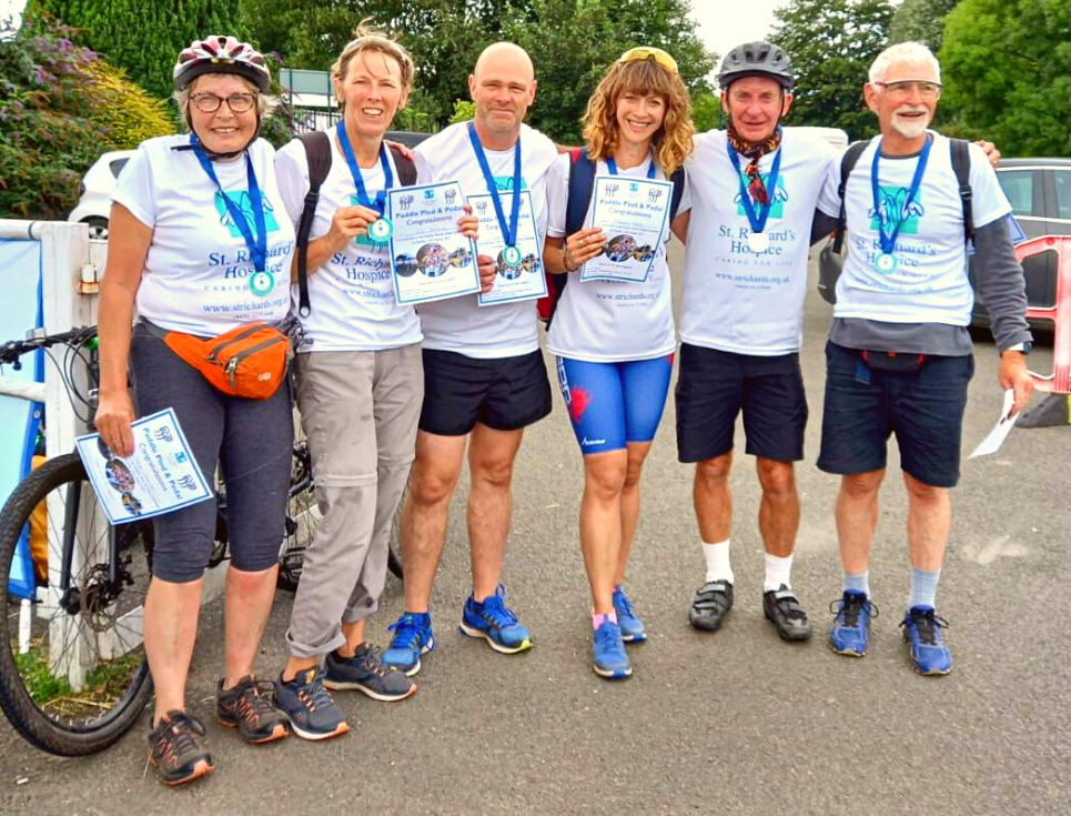 A group of people in sports wear and white St Richard's branded t-shirts stand together wearing Paddle, Plod and Pedal medals.