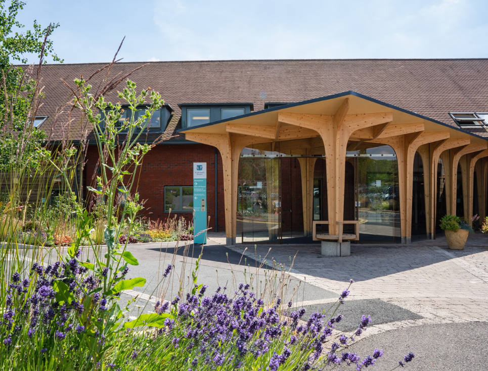 Wooden and glass entrance to hospice building, flower border to the left.