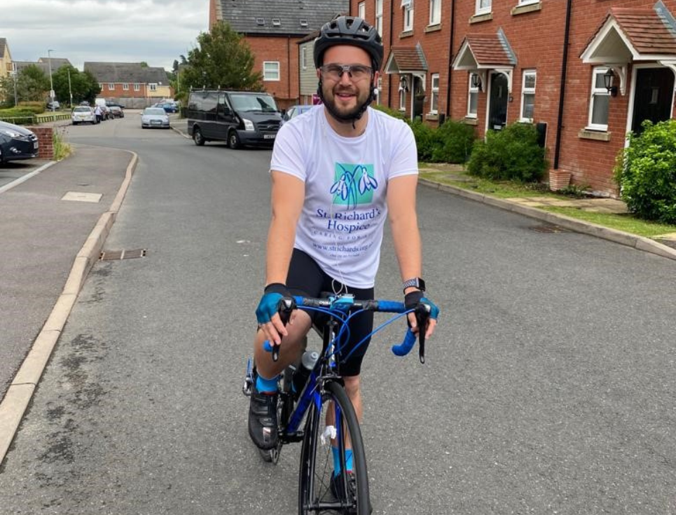 Mark Breakwell sits on his bicycle wearing a St Richard's Hospice branded t-shirt and cycling helmet.