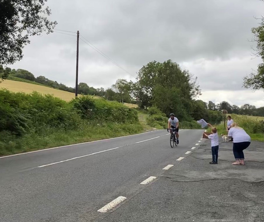 Mark Breakwell cycles along a road, while people cheer him on.