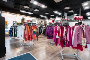 The inside of the St Richard's Hospice Malvern Link Department Store. Rails of clothing is on display, coordinated by colour.