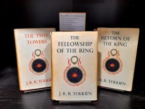 Three volumes of the Lord of the Rings stand on display inside a black cabinet. The books' dust jackets are cream with a red and black image beneath each title.