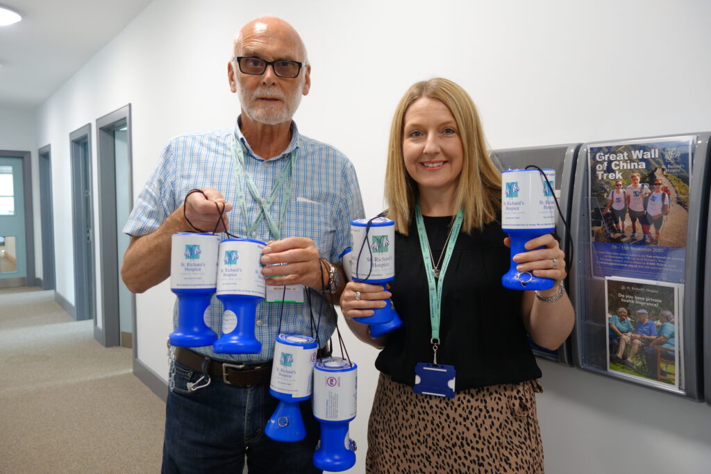 Two people stand together in a corridor at St Richard's Hospice holding collection tins.