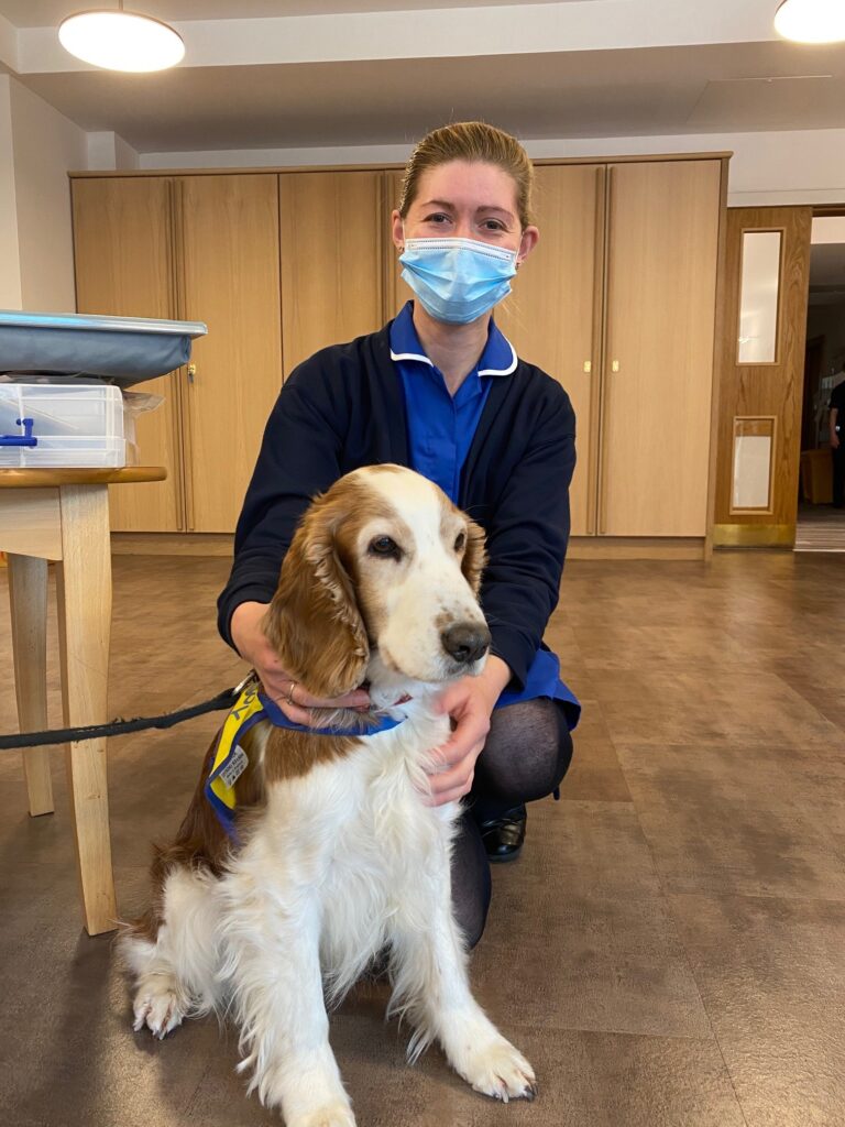 A hospice nurse sits with a brown and white springer spaniel in the hospice's Living Well Centre.