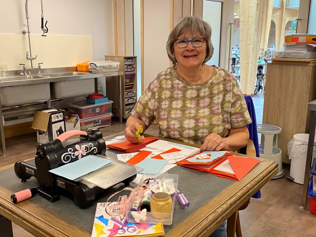 Volunteer Jenny sits at a desk in the hospice's Creative Therapy room, with art supplies in front of her. 