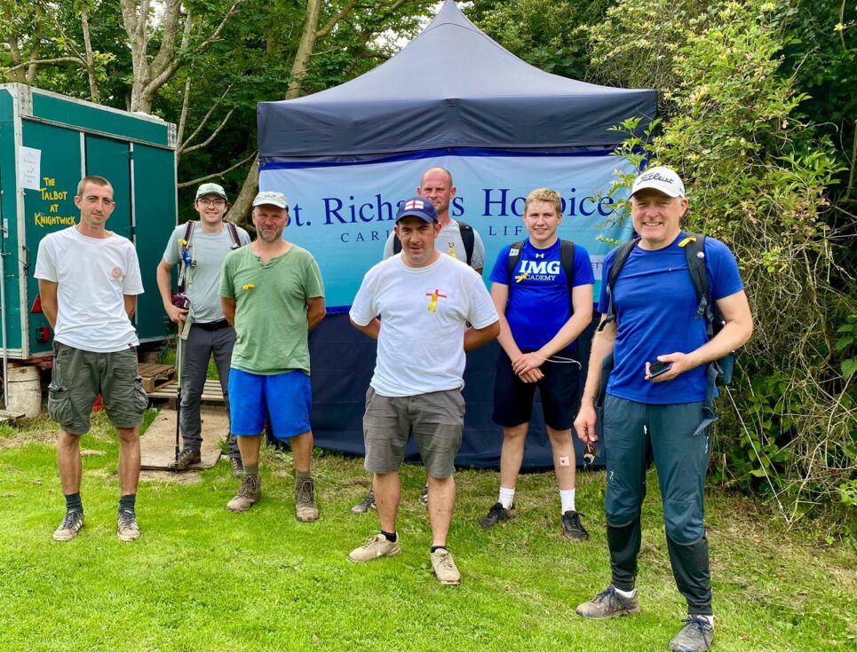 A group of walkers stand together in front of a blue marquee featuring a St Richard's Hospice banner.