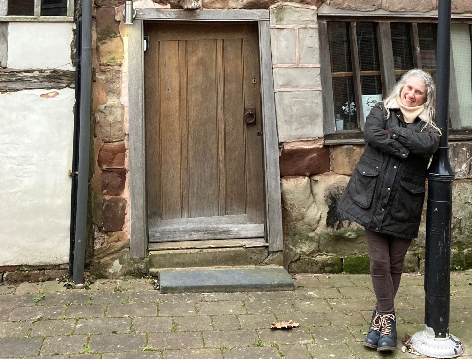 woman in walking clothes leaning against a lamp post in front of a historic house