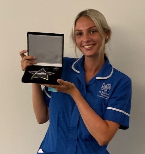 Lydia with her Cavell Star Award. She is wearing her blue nurses' uniform and smiling.