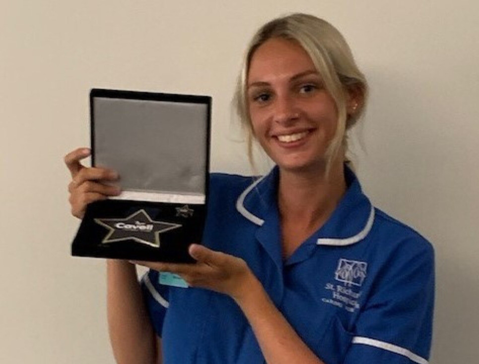 Lydia pictured with her Cavell Star Award. She is wearing her blue nurses' uniform and is smiling.