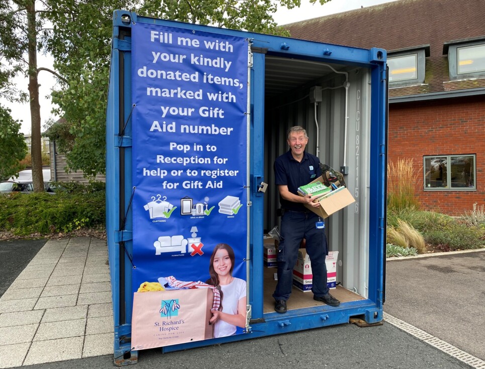 Tom stands inside a large, blue shipping container holding a box of donated items.