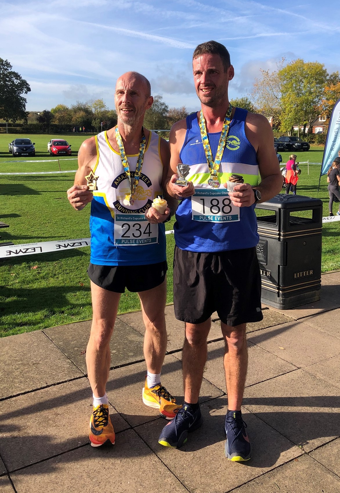 Two runners stand together with their cupcake chase medals and cake.