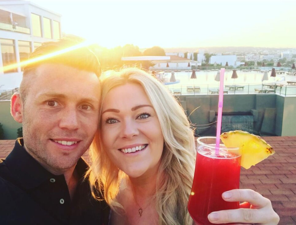 Andy and Hayley take a selfie during a sunset. Hayley holds a cocktail.