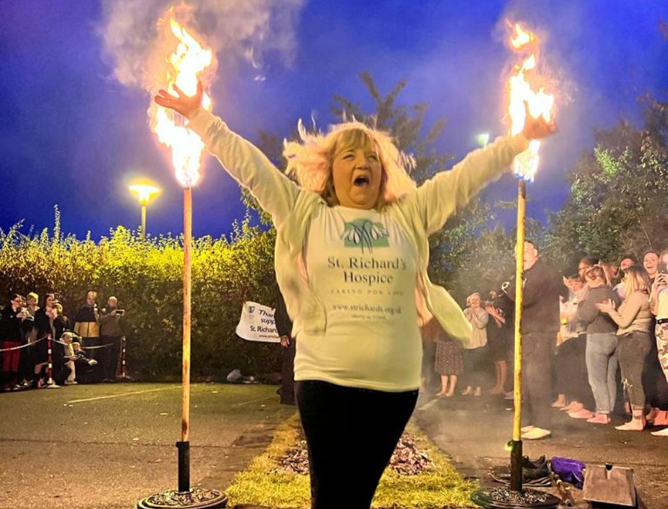A woman with blond hair, with her hands in the air after completing the 2023 fire walk in aid of St Richard's Hospice