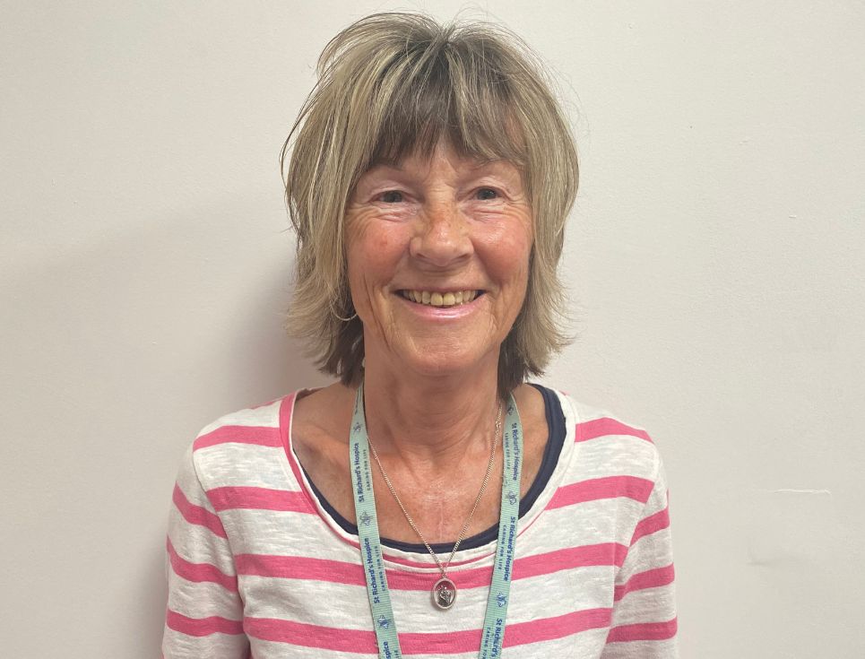 Anne pictured against a plain white wall. She is smiling and wearing a pink and white striped t-shirt.