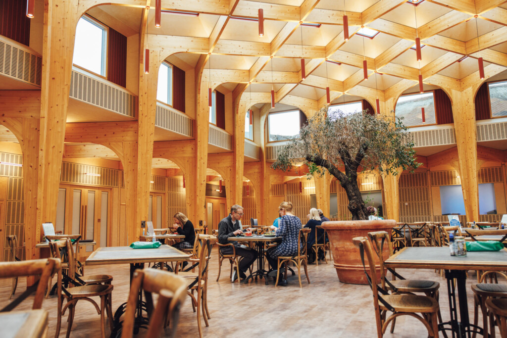 The Green, a large open social and cafe space at the heart of St Richard's Hospice. People sit at cafe tables enjoying lunch and cups of coffee.