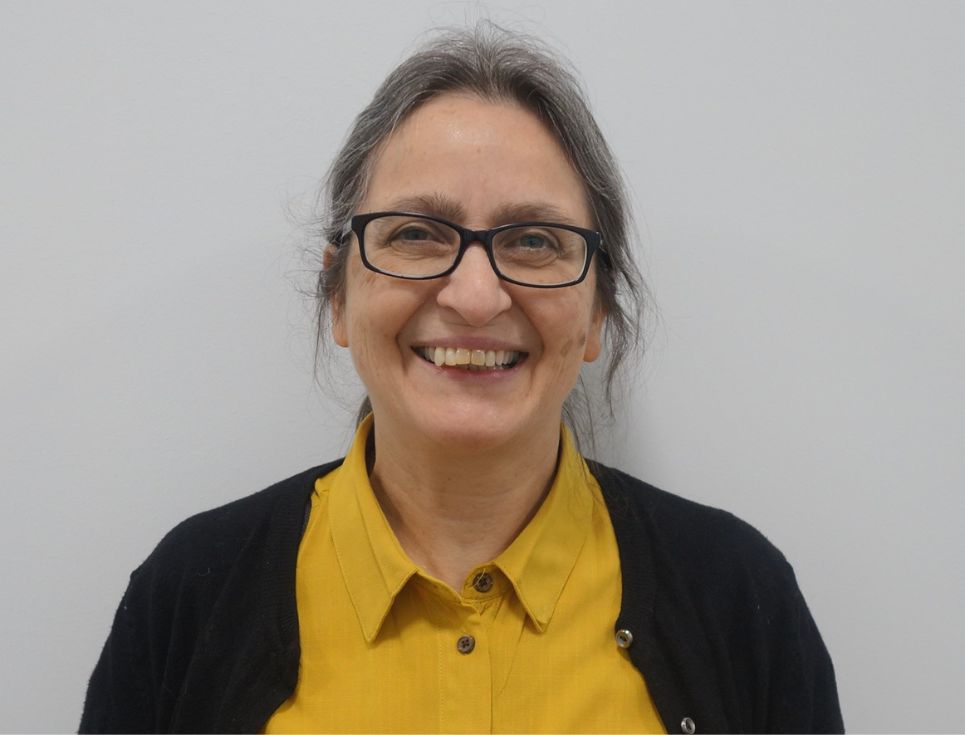 Safia Sawal pictured against a plain white background. Safia wears a yellow top and black cardigan. She is smiling.