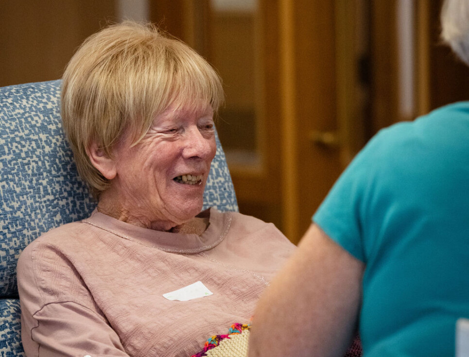 A person sits in a comfy chair in the hospice's Living Well Centre. They are smiling.