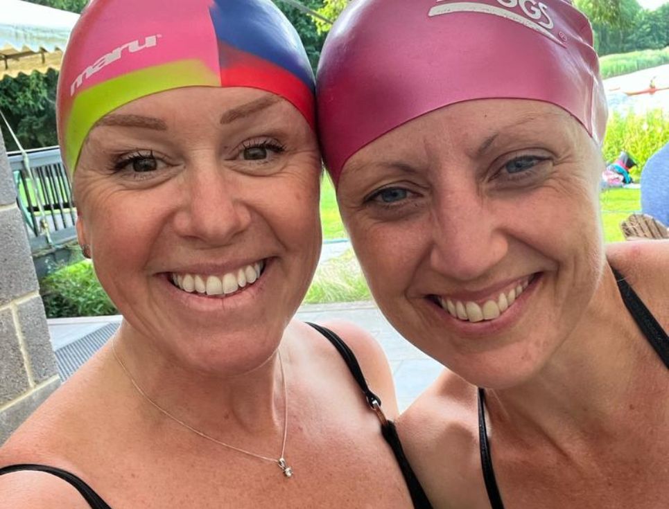 Two women dressed in swimming costumes and swim caps smiling.