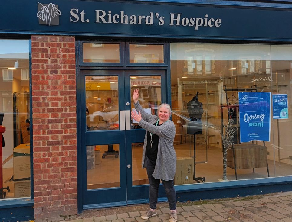 Shop manager Esther stands outside the new Barnards Green shop. Through the windows, you can see the shop fitting is underway. Esther stands smiling outside with her arms outstretched towards the sign, which reads St Richard's Hospice.