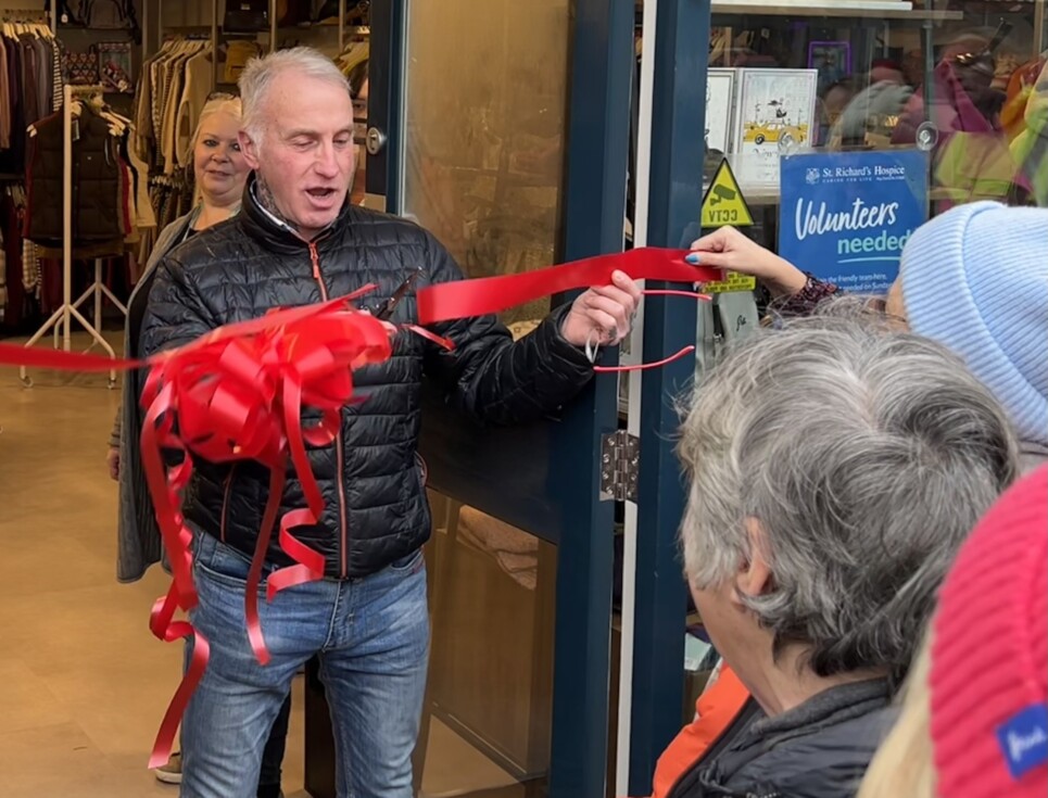 Man cuts red ribbon across door opening to mark the opening of the new shop