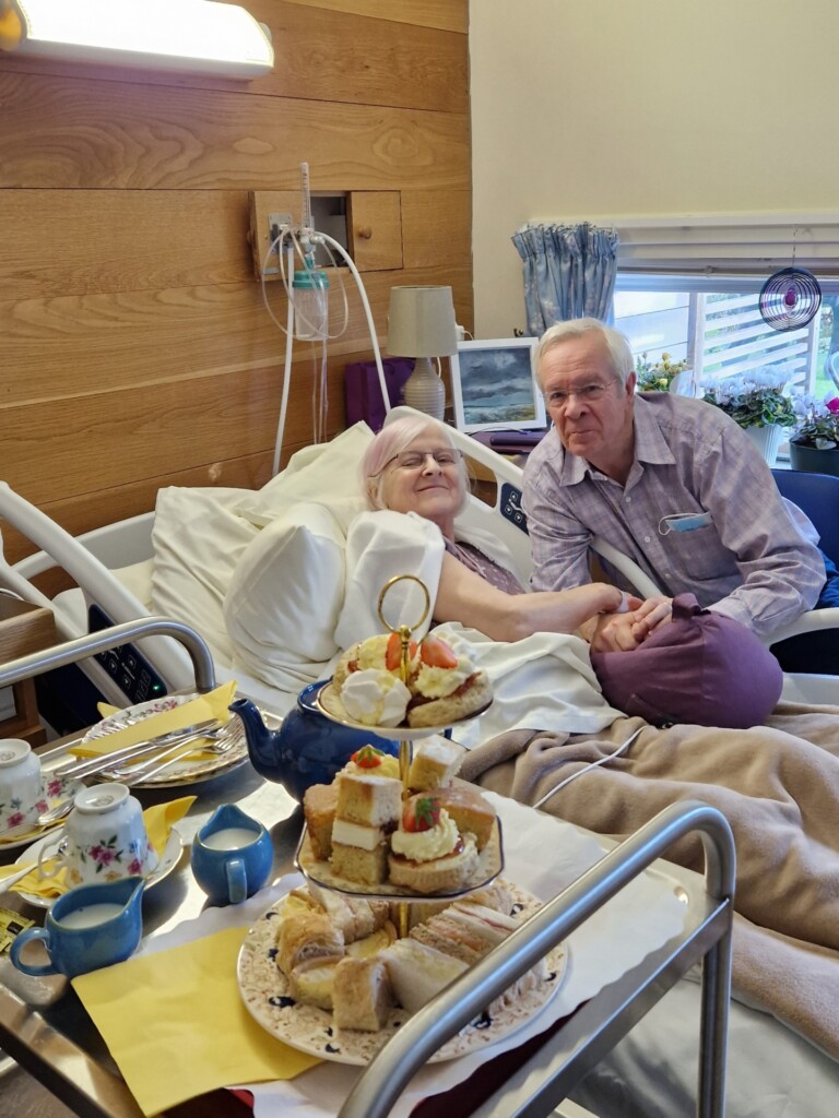 Vanessa in bed at the hospice, with her husband Ian by her side. In the foreground is a trolley filled with cakes and tea for the couple.