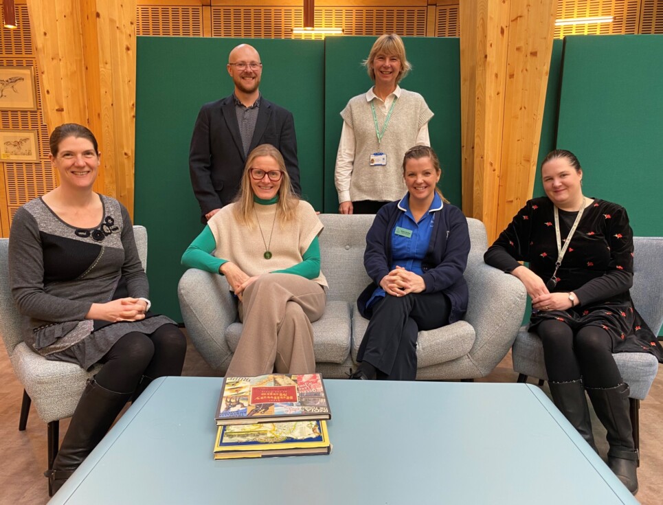 The Education Team at St Richard's Hospice. The team of six people sit together on comfy chairs in The Green at St Richard's. Two of the team stand behind the rest. Everyone is smiling.