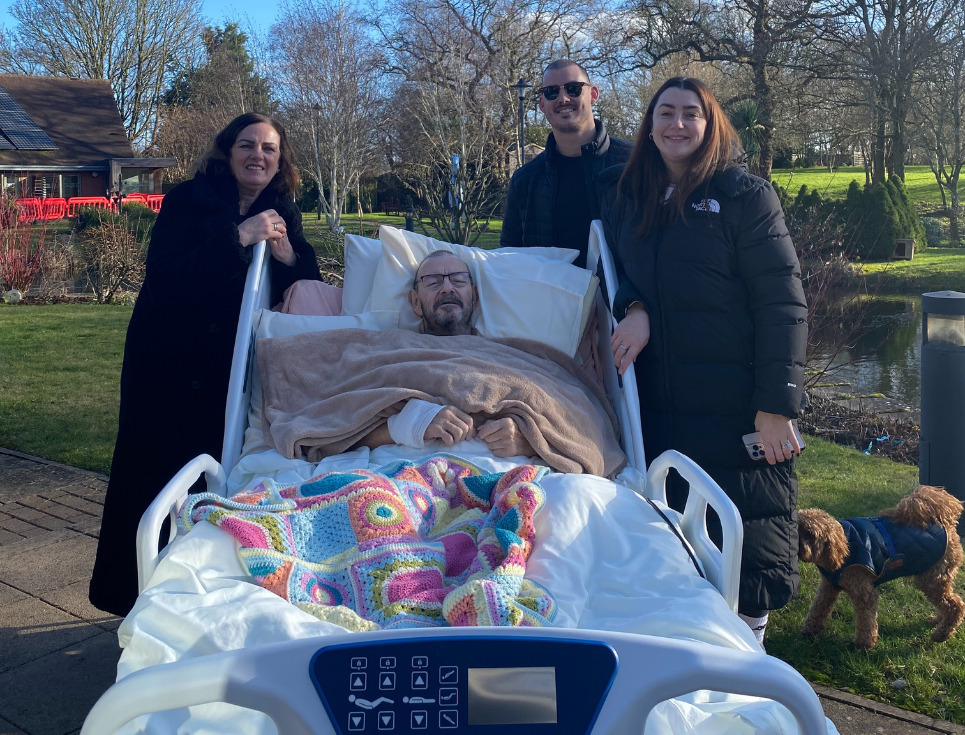 Ray, pictured in bed in the hospice's gardens on a bright blue-skied day. Around him are his family, including his wife and children.