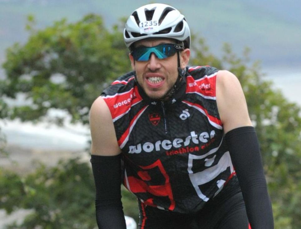 A man cycling in a cycling helmet, jersey and sunglasses.