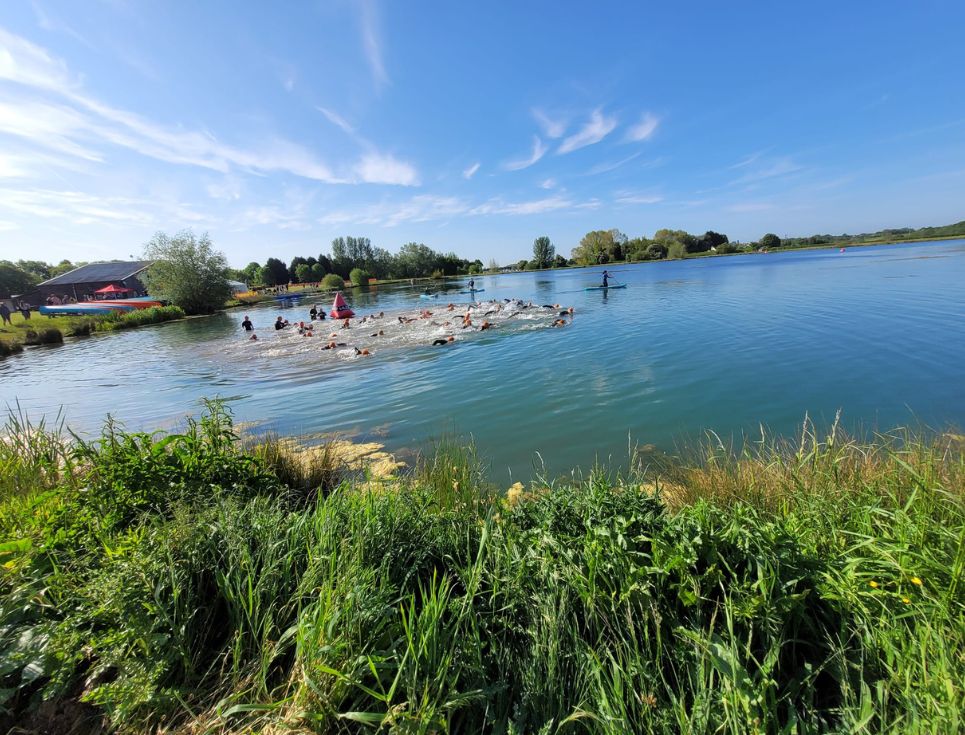 A group of swimmers, swimming in a blue lake as part of a triathlon.