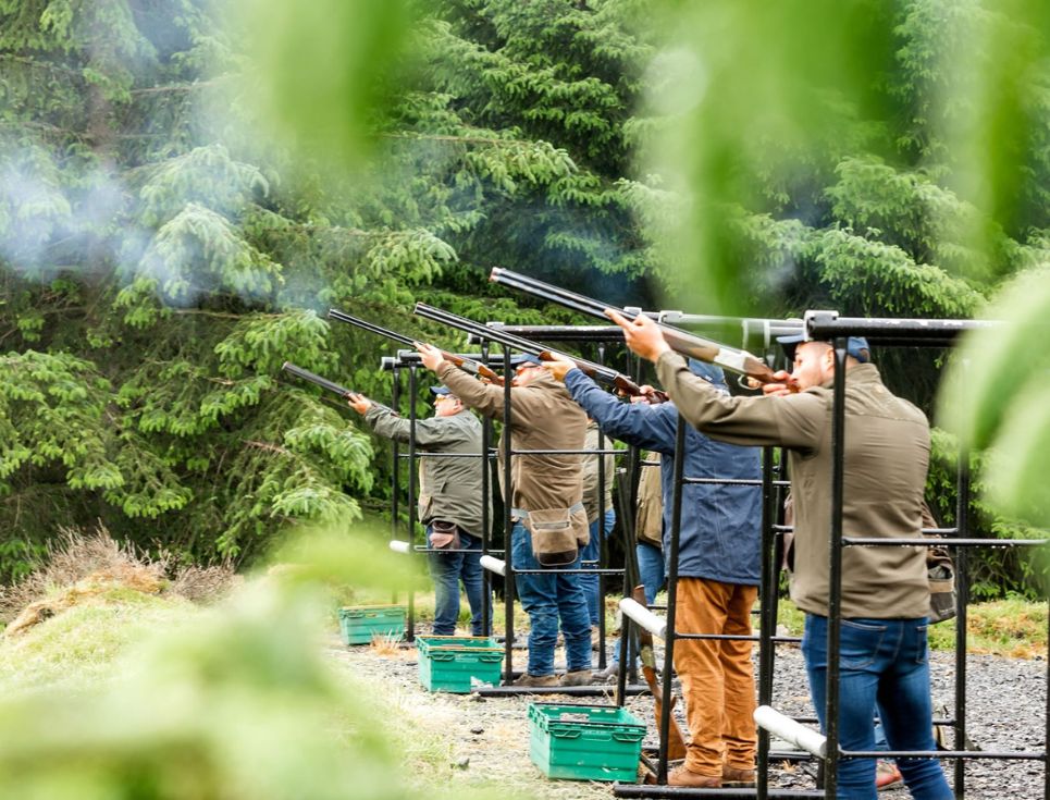 A group of men taking aim to shoot at clay pigeons.