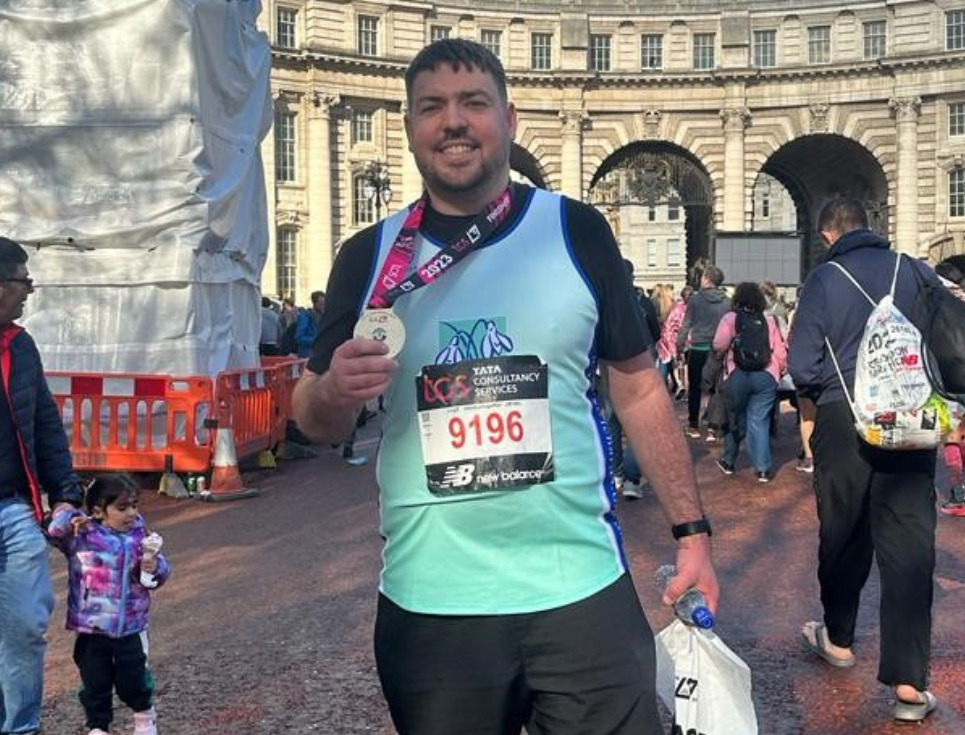 James pictured in his running gear holding his London Marathon medal and smiling.