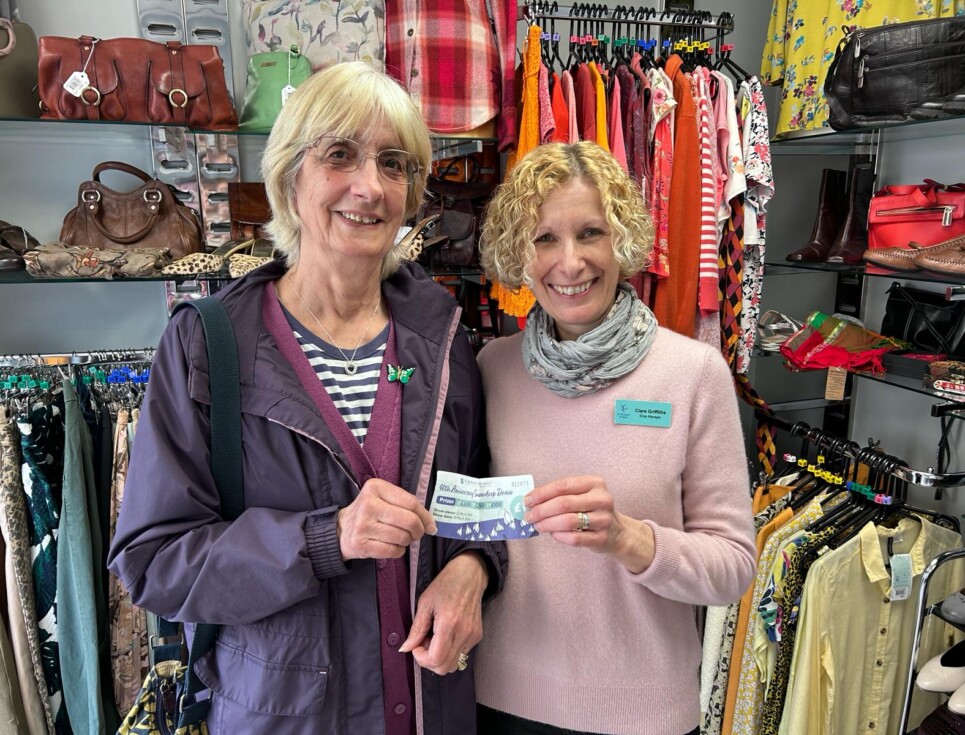 Two women standing in a St Richard's charity shop, both holding the end of a raffle ticket.