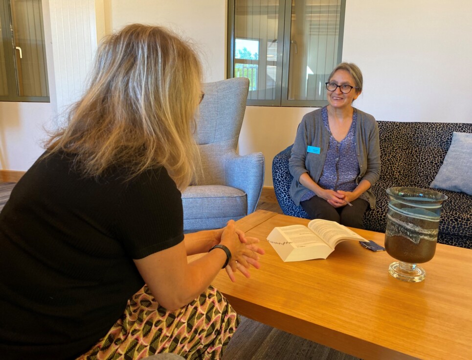 Safia speaks to a person around a coffee table at the hospice.