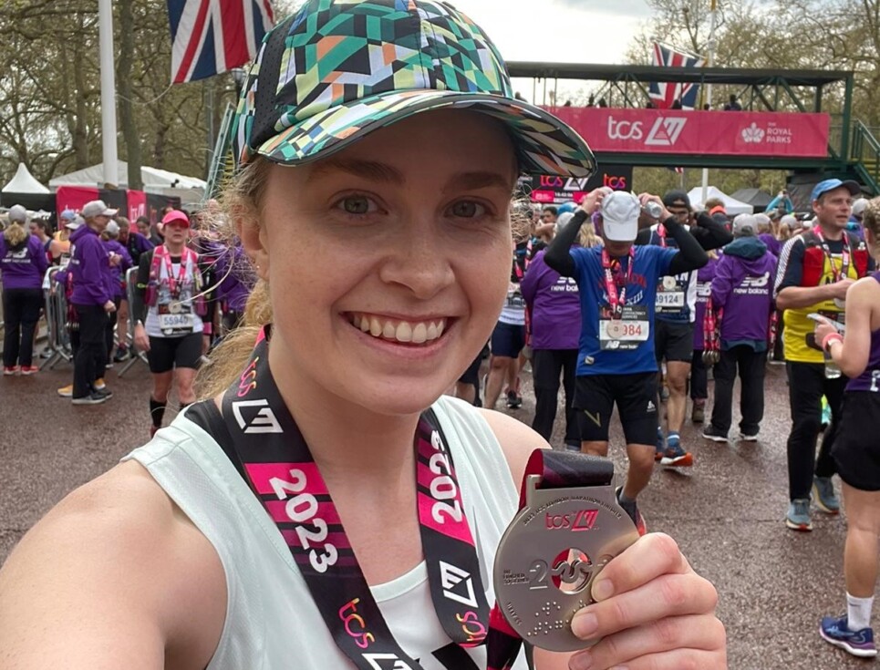 Skye pictured after finishing the London Marathon. She is wearing a white running vest, green patterned baseball cap and her London Marathon medal. She is smiling.