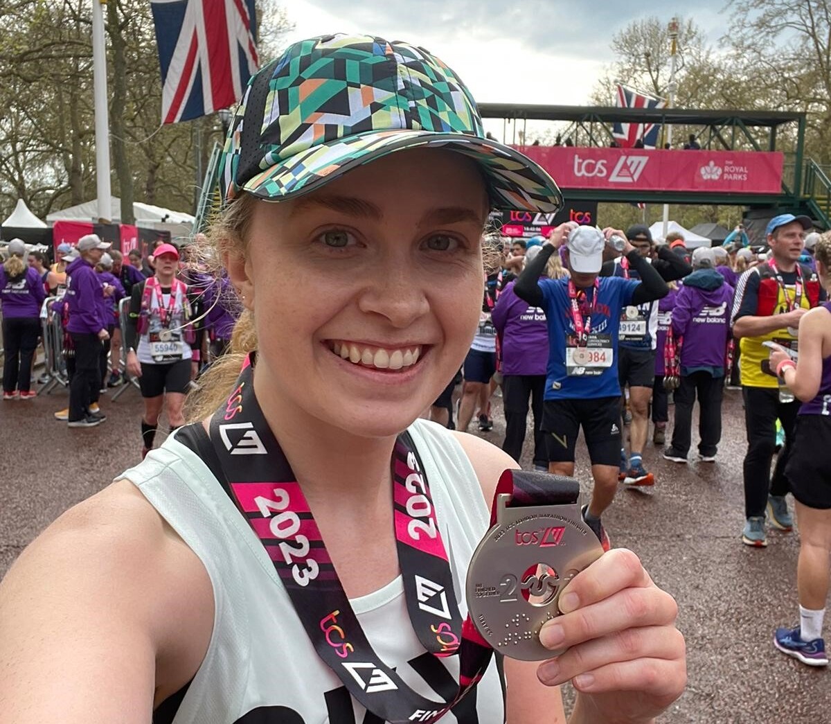 Skye pictured after finishing the London Marathon. She is wearing a white running vest, green patterned baseball cap and her London Marathon medal. She is smiling.