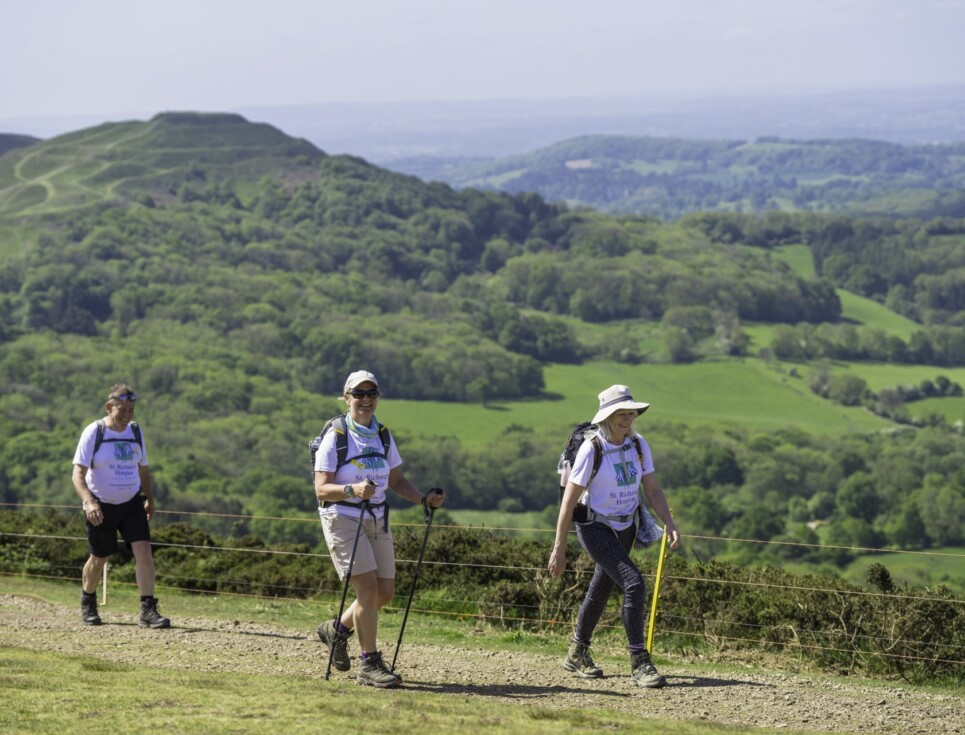 Walkers striding across the Malvern Hills wearing St Richard's Hospice t-shirts on a sunny, blue skied day.