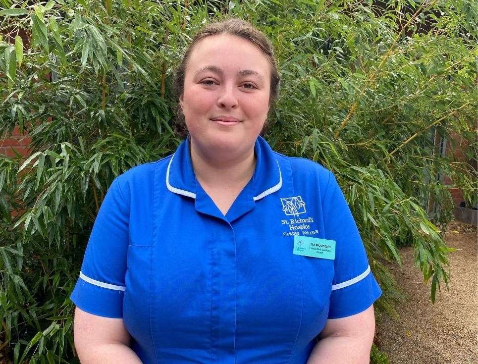 Tia pictured in the hospice garden wearing a bright blue nurses' uniform.