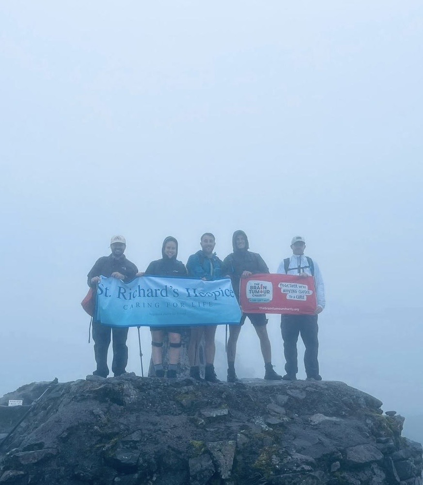 A group of people holding banners stand at the summit of a mountain. They are surrounded by thick mist.