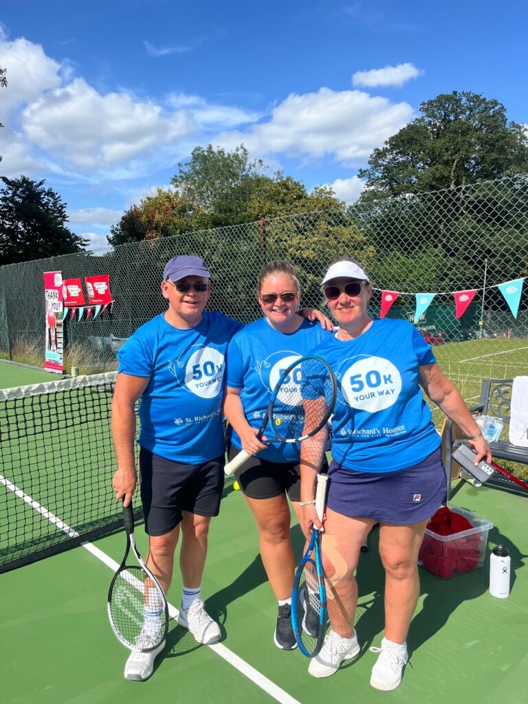 Three people holding tennis rackets on a court in the sunshine.