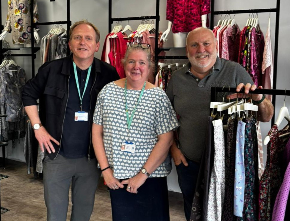Simon, Michelle and Dan stand together in the new superstore. They are standing by rails of clothing and smiling.