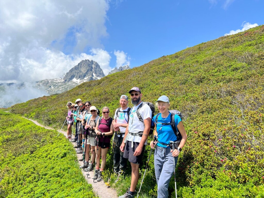 A group of walkers stood on a footpath on the side of a green hill.