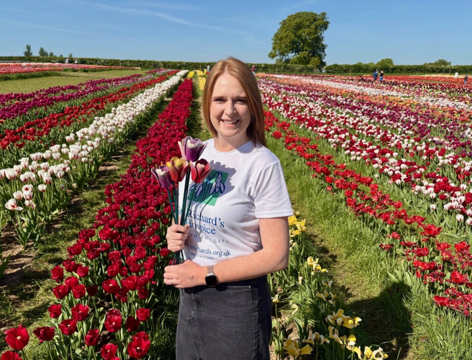 A hospice fundraiser stands in a field of tulips holding some St Richard's Hospice tulip sculptures