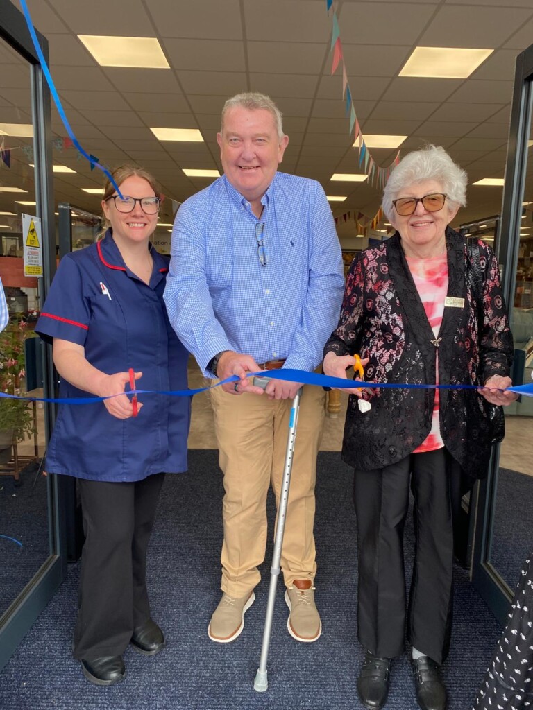 Three people stand behind a blue ribbon, ready to cut it and officially open the superstore.